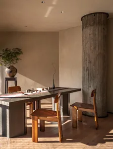 A warm-toned interior design featuring wooden furniture and concrete columns, with sunlight streaming in.