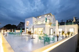 Modern minimalist exterior with white stucco, glass windows, and green furniture under a twilight sky.