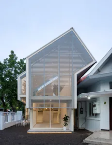 A modern house exterior with a glass wall and roof, featuring a small plant and outdoor seating area.