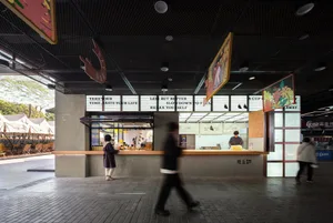 A minimalist restaurant interior features a concrete and wood counter, with a glass panel above displaying colorful artwork.