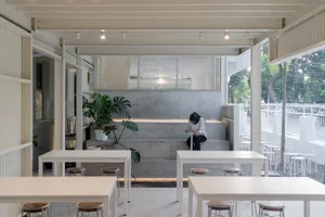 A minimalist cafe interior featuring concrete walls and wooden furniture.