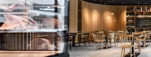 Modern restaurant with wooden tables and chairs, stainless steel appliances, and wine bottles on shelves.