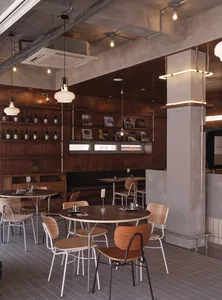 Industrial-style restaurant interior with wooden tables, metal chairs, and concrete walls.