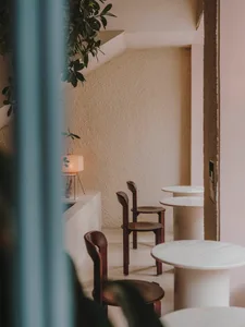 Minimalist cafe with round marble tables and wooden chairs, featuring textured walls and indoor plants.