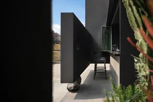 Concrete patio with a modern bar setup featuring metal stools and a countertop with a window.