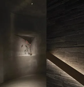 A minimalist interior space featuring dark stone walls and a wooden beam illuminated by a spotlight