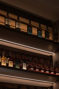 A well-lit bar wall with wooden shelves displaying various bottles of alcohol.