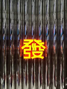 A neon sign featuring the Chinese character '發' (fa), meaning 'fortune' or 'prosperity', displayed against a metallic, reflec