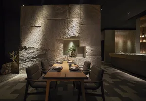 A modern dining room with a stone wall and table set for dinner.