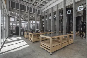A spacious industrial coffee shop with concrete flooring, wood tables, and large glass windows.