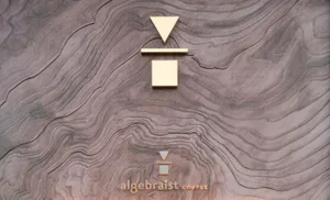 A sign with geometric shapes made of copper, bronze, and gold on a wooden texture background.