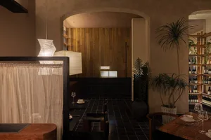 Industrial-style restaurant interior with exposed concrete ceiling, wood-paneled walls, and black-tiled floor.