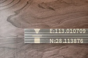 A minimalist building exterior featuring a wooden texture with a metal plaque displaying coordinates.