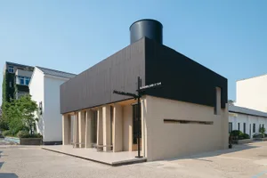 A modern, minimalist coffee shop with a concrete exterior and a large, black cylindrical roof vent.