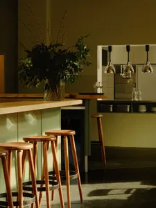A modern kitchen with wooden stools, green cabinets, and a vase of flowers.