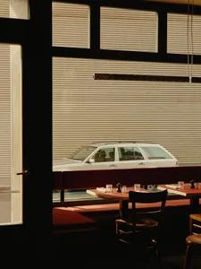A cozy restaurant booth with red upholstery, wooden tables, and a large window with blinds, showcasing comfortable seating an