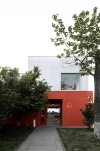 A modern building with a red exterior, white facade, and a tree in the foreground.