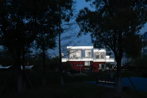 一棟現代房屋，擁有白色板材外牆與紅色底層，夜間燈光照亮。