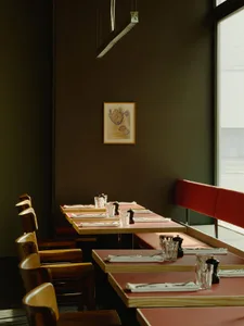 Framed drawing of chicken hanging above a restaurant table setting with wooden chairs, white plates, and glasses.