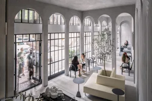 An industrial-style restaurant interior with concrete arches and large windows.