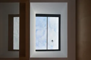 A window view with an airplane flying in the blue sky.