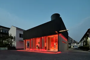Modern storefront with a shimmering black exterior and red neon lighting on a twilight sky background.