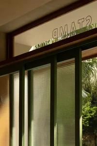 A modern glass door with a textured pattern, seen from the inside looking out towards a tropical garden.