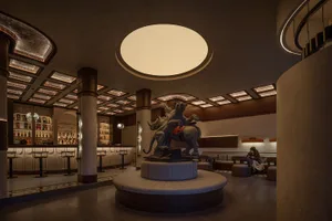 A modern industrial restaurant interior with a concrete ceiling and floor, featuring a statue of a lion and lioness riding a 