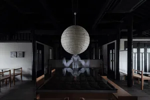 A modern restaurant interior featuring a hanging round paper lamp, wooden furniture, and a glass countertop.