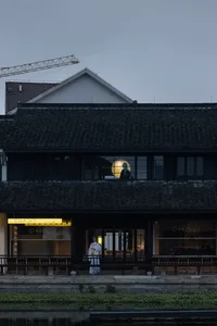A traditional retail storefront with brick walls and a tiled roof, featuring a person standing in front of the entrance.