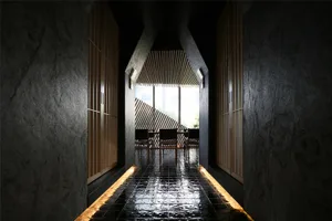 A minimalist waiting area with concrete walls, wood furniture, and a view through a tall window.
