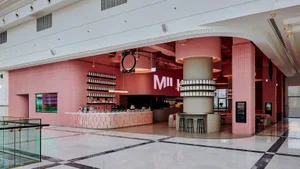 A modern café interior with pink tiled walls, a steel counter, and industrial lighting fixtures.
