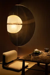 A modern tea room with a circular light fixture, wooden table, and minimalist furniture.