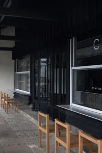 Outdoor seating area of a retail storefront featuring black exterior walls and wooden chairs.