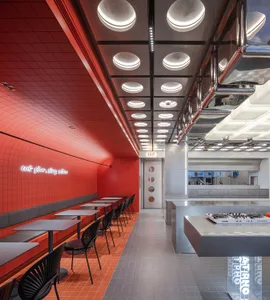 A modern restaurant interior with red tiled walls, black chairs, and white tables.
