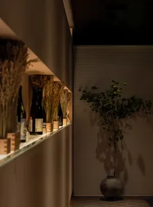 Modern minimalist restaurant interior featuring wooden accents, shelf with bottles, and green plant.