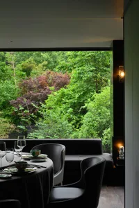 Modern restaurant with glass windows overlooking greenery, featuring a contemporary design with sleek black furniture and gre
