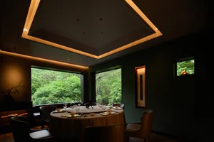 Modern restaurant interior with green leather seating and green glass windows showcasing lush greenery outside.