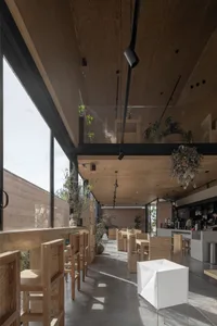 Modern cafe interior with wooden furnishings, large windows, and hanging plants.