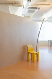 Modern, minimalist interior design featuring a bright yellow chair and a curved wooden desk.