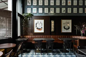 Restaurant interior with dark wood tables, black leather seating, and industrial artwork on the walls.