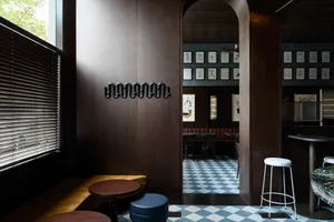 Modern restaurant interior with wooden seating, marble tables, and checkered-tiled floor.