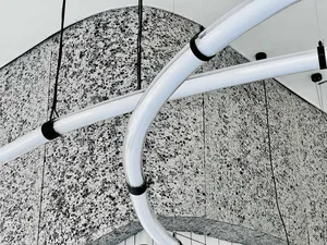White metal pipes suspended from the ceiling in an industrial setting with concrete walls.