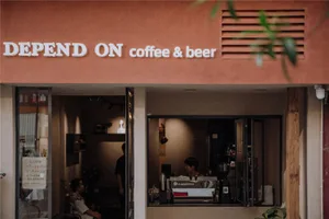 紅土泥牆的店面，招牌寫著「DEPEND ON coffee & beer」。
