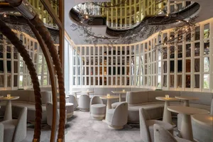 A modern restaurant bar with sleek, curved seating, round tables, and glass walls.