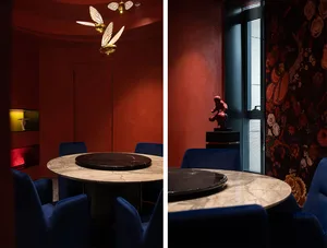 Round marble tables with blue velvet chairs in a modern restaurant interior with floral wallpaper and decorative statues.