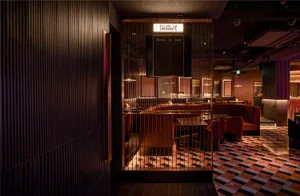 A modern restaurant interior with metallic wood walls, checkered tile flooring, and warm ambient lighting.