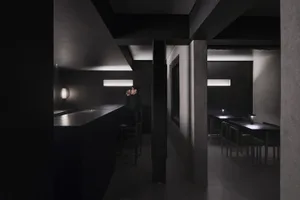 A minimalist restaurant interior with black concrete walls and lighting fixtures