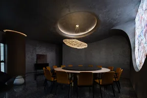 Modern conference room featuring a round table surrounded by chairs, with a chandelier, marble floor, and concrete walls.
