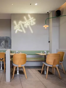 Modern industrial restaurant interior with neon signage and green booth seating.